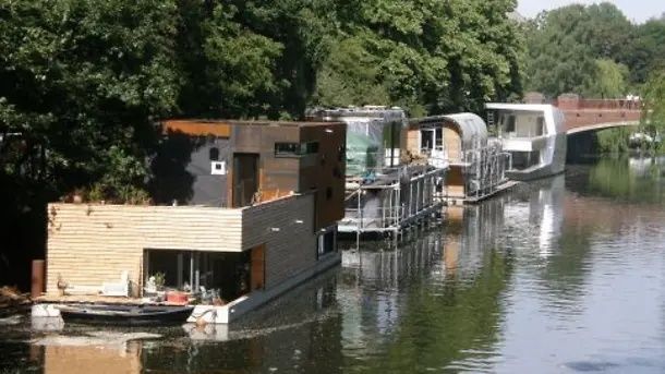 Mehrere schwimmende Gebäude und Boote liegen dicht an einem bewaldeten Flussufer.