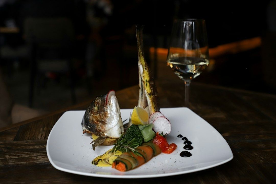 Gegrillter Fisch mit Gemüse und Weißwein auf einem gedeckten Tisch